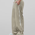 Man in light khaki baggy wide leg sweatpants, side view, showing stripe detail and loose fit. White sneakers.