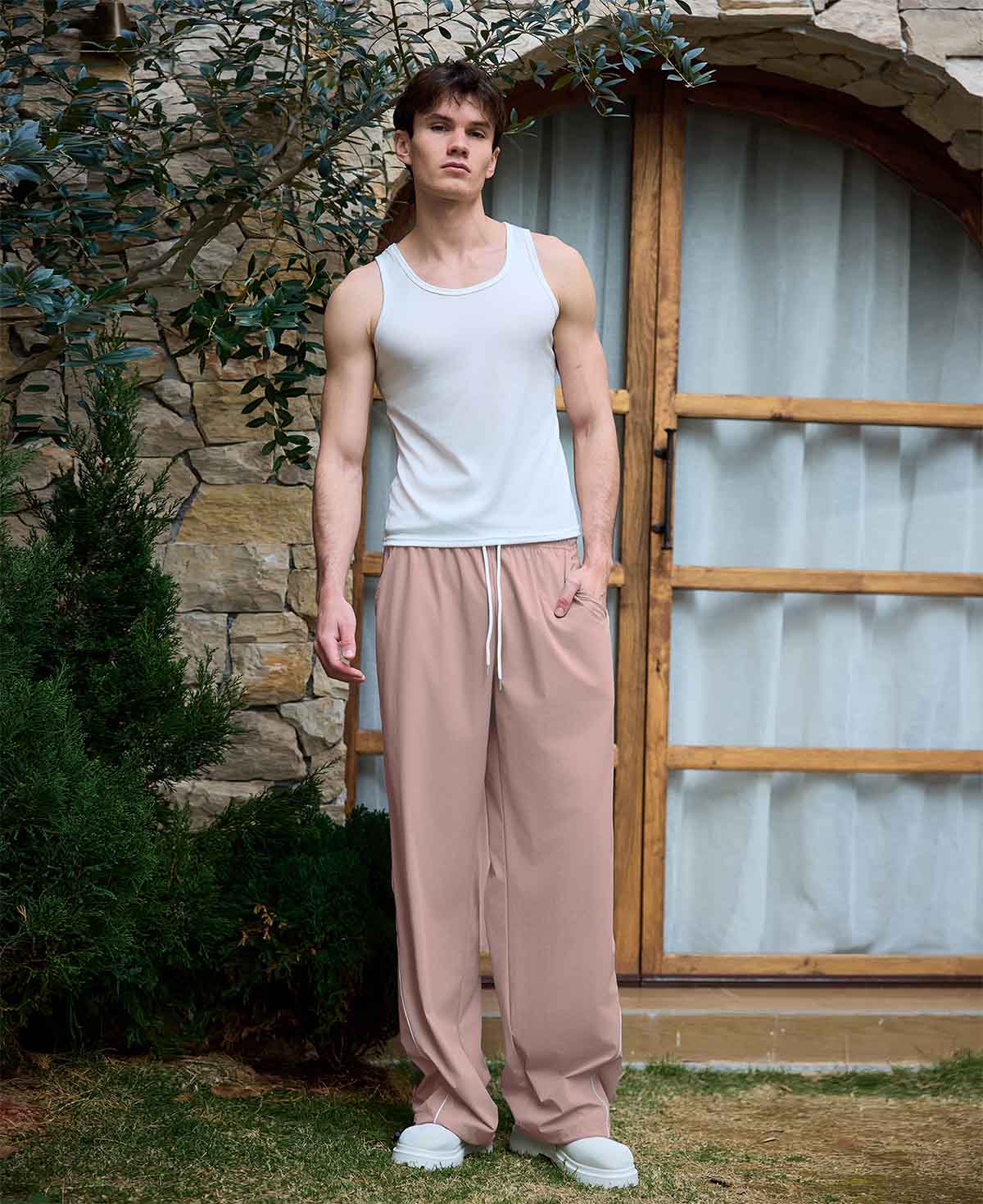 Full view of man wearing pink baggy wide leg sweatpants, white sneakers, front stance, showing overall look.