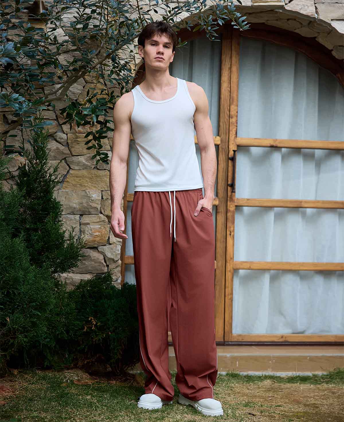 Full view of man wearing red baggy wide leg sweatpants, white sneakers, front stance, showing overall look.